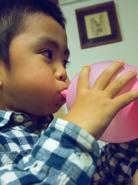 Photo of a child blowing up a balloon with effort by Norihiro Kataoka.